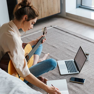 Image Of Young Woman Writing Notes While Playing Acoustic Guitar At Home